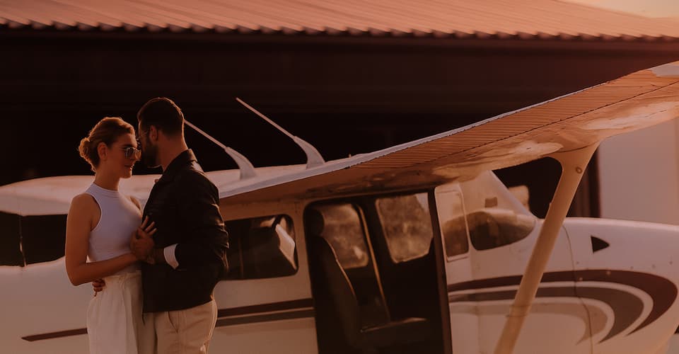 A pilot and passenger beside a small airplane on the ramp at Van Nuys, the passenger putting on a headset