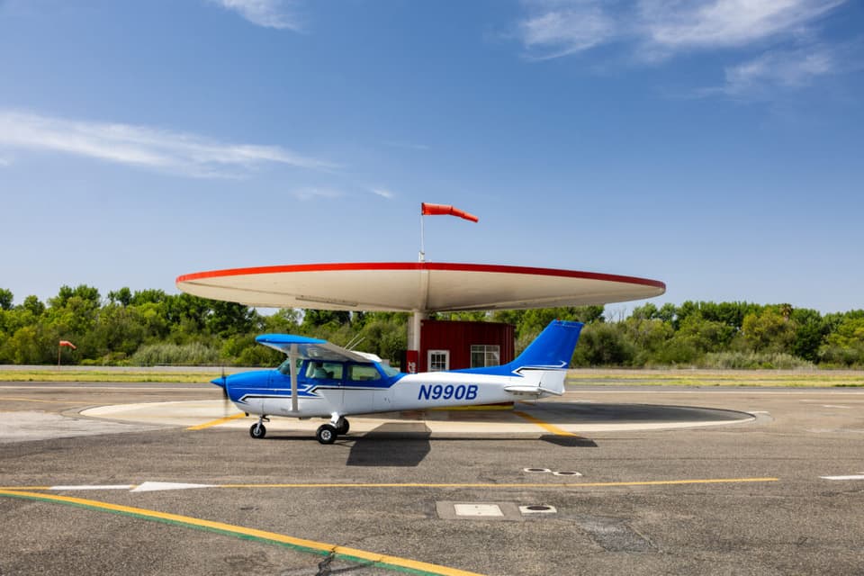 Fly LA Experience Cessna N990B on the ramp under a blue sky with scattered clouds, a windsock showing the breeze